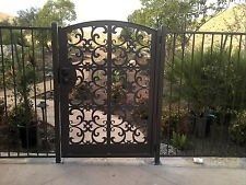 Black wrought-iron gate with ornate scrollwork in a garden walkway.
