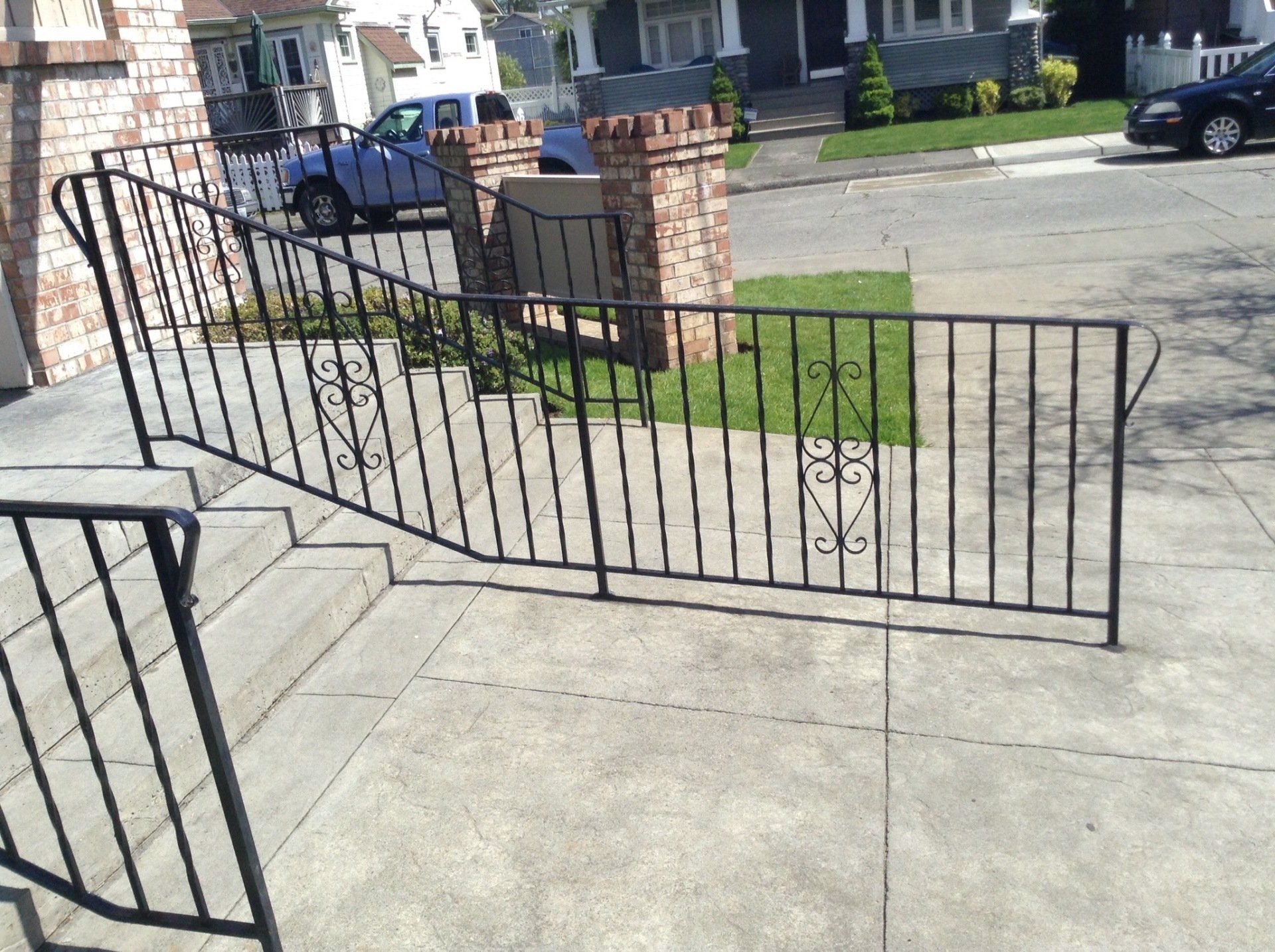 Black metal accessibility ramp and railing leading up concrete steps outside a house.