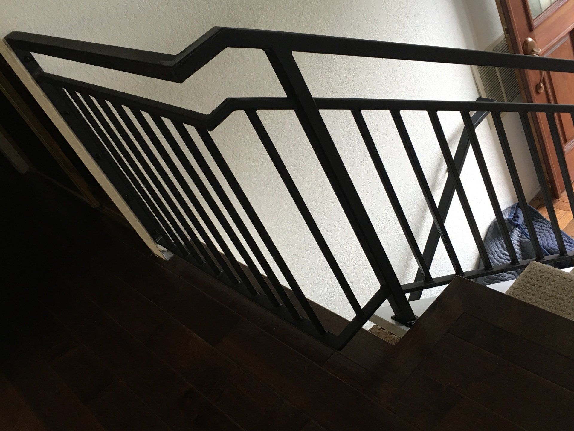 Black metal stair railing beside a dark wooden staircase landing with white walls