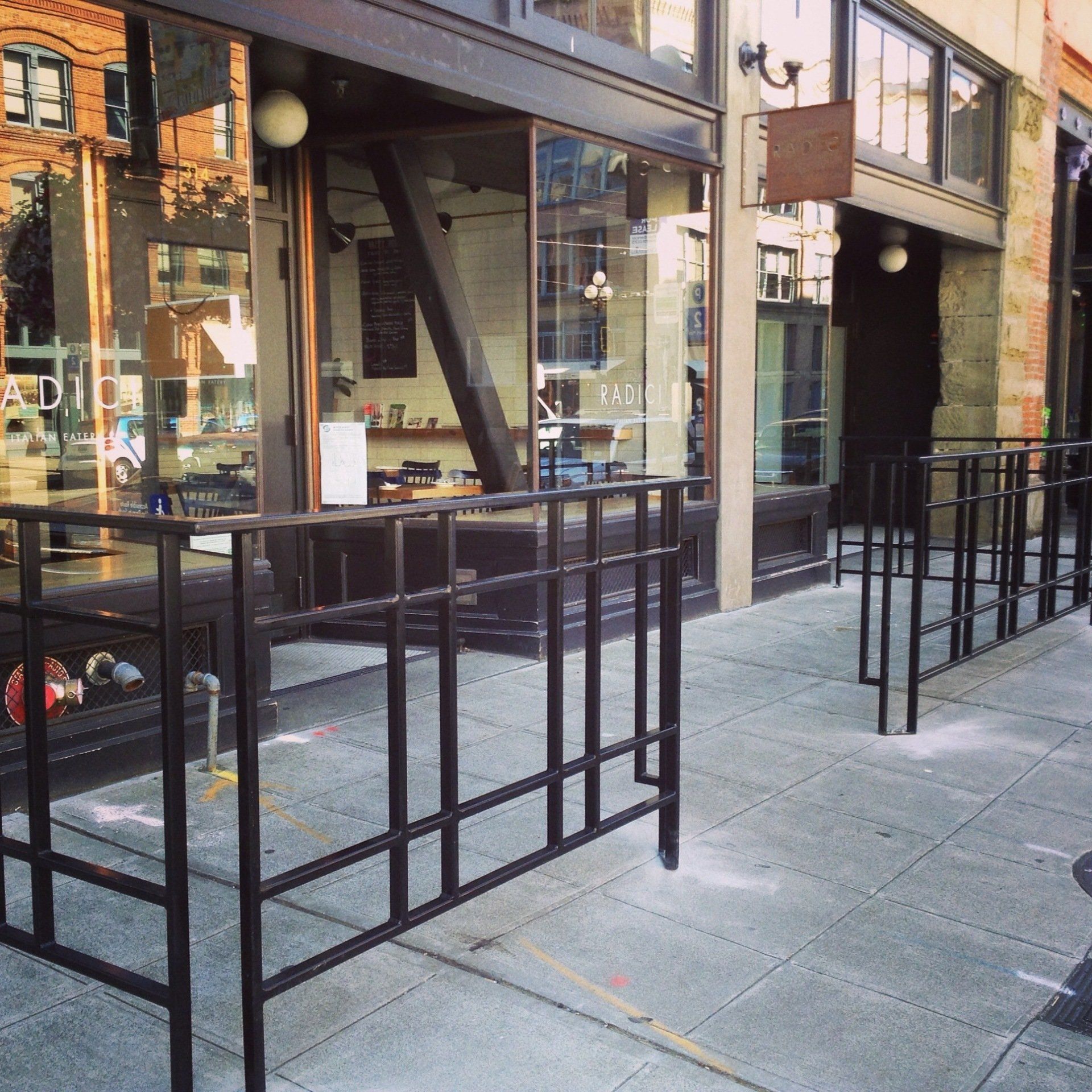 Outdoor sidewalk café with black metal railings and large storefront windows on a city street