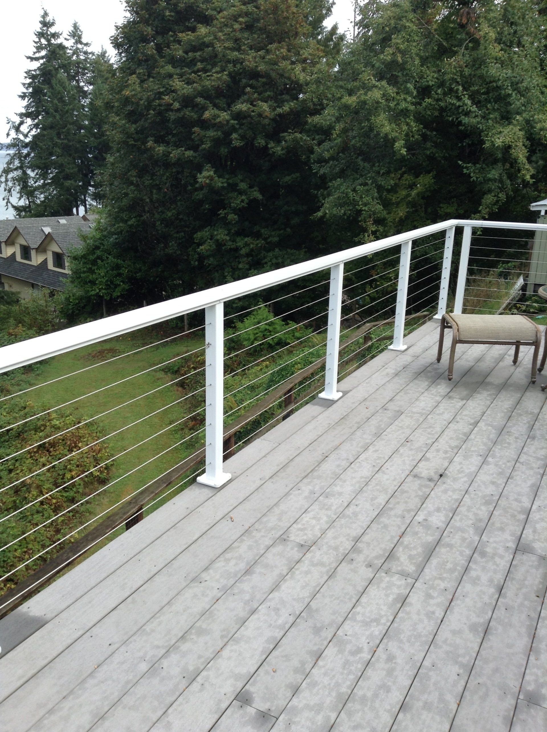 Wooden deck with white cable railing overlooking trees and a distant house
