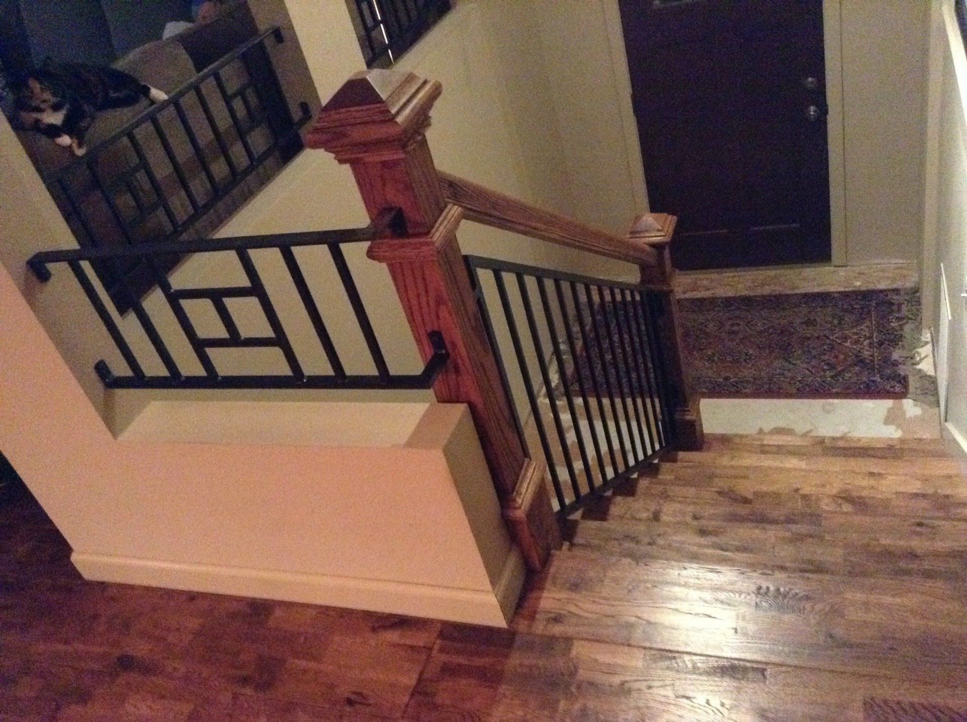 Wooden staircase with black railing and red newel post beside a landing and hallway