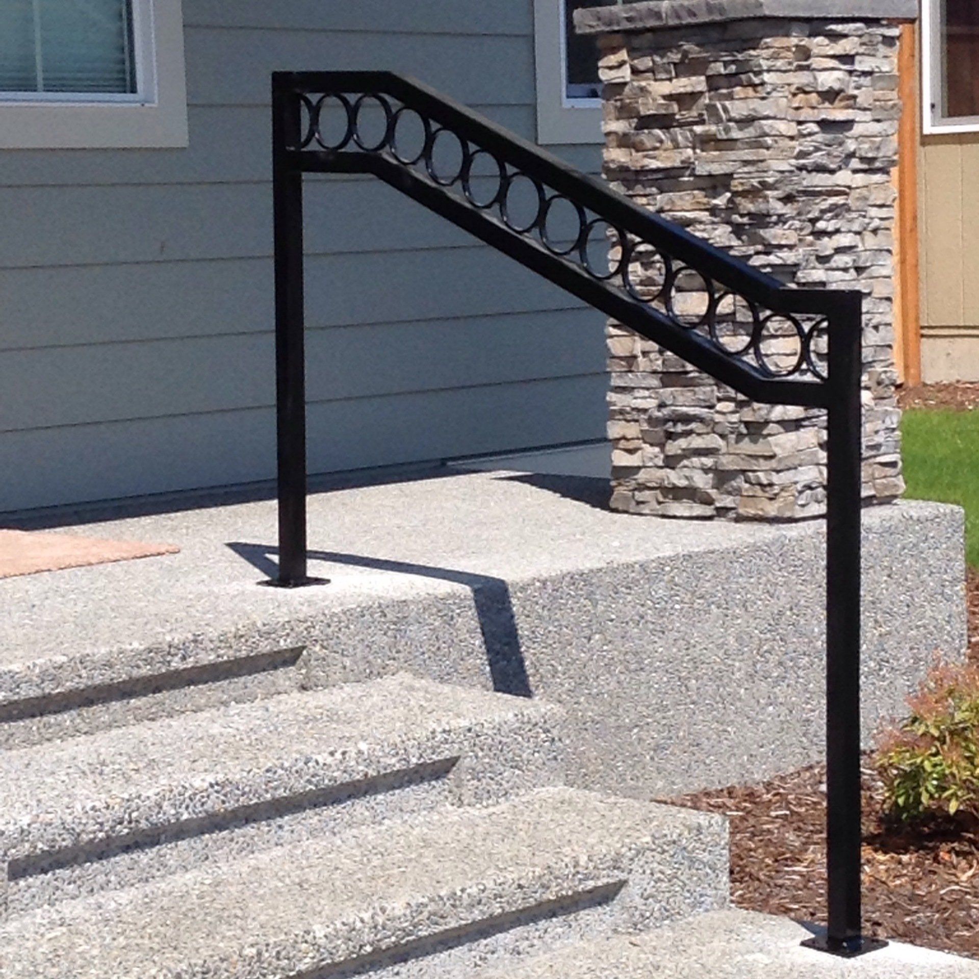 Black metal stair railing with circular decoration beside concrete steps and stone wall.