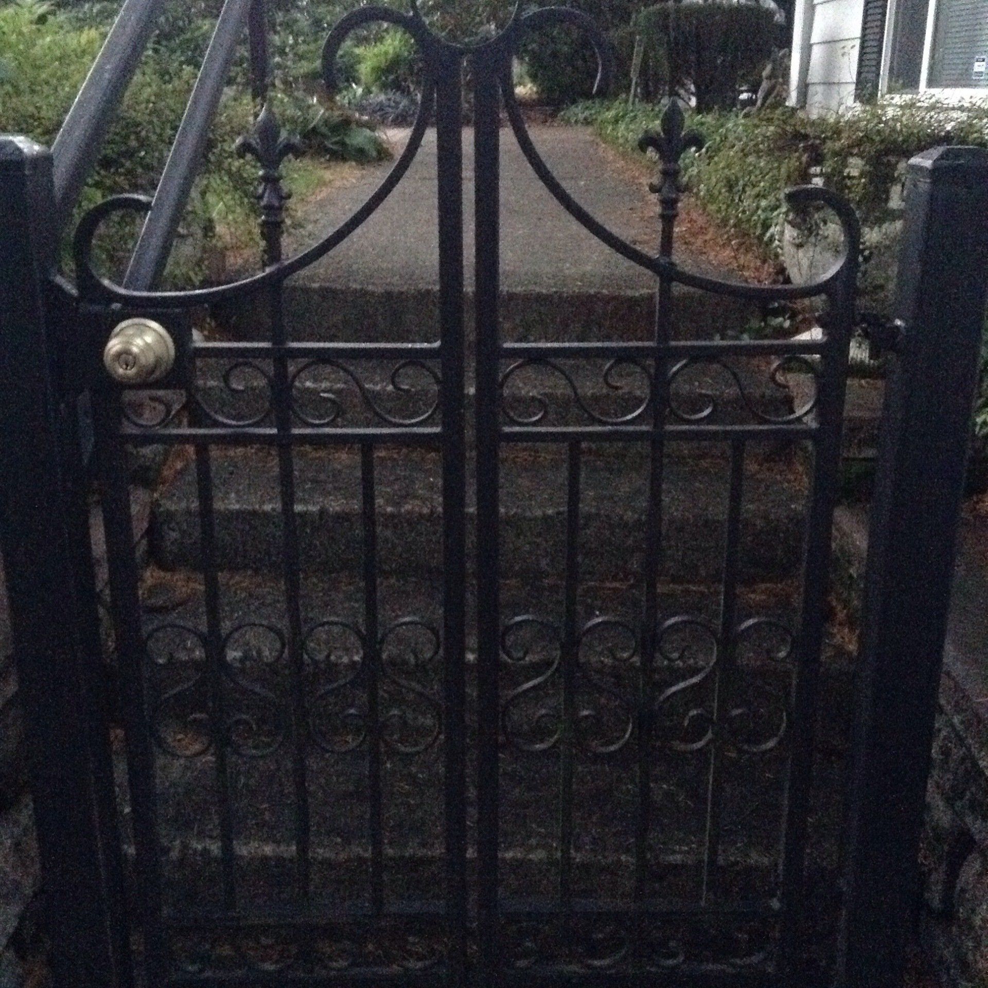Black wrought-iron garden gate with decorative scrollwork and a brass knob at the entrance to stone steps.
