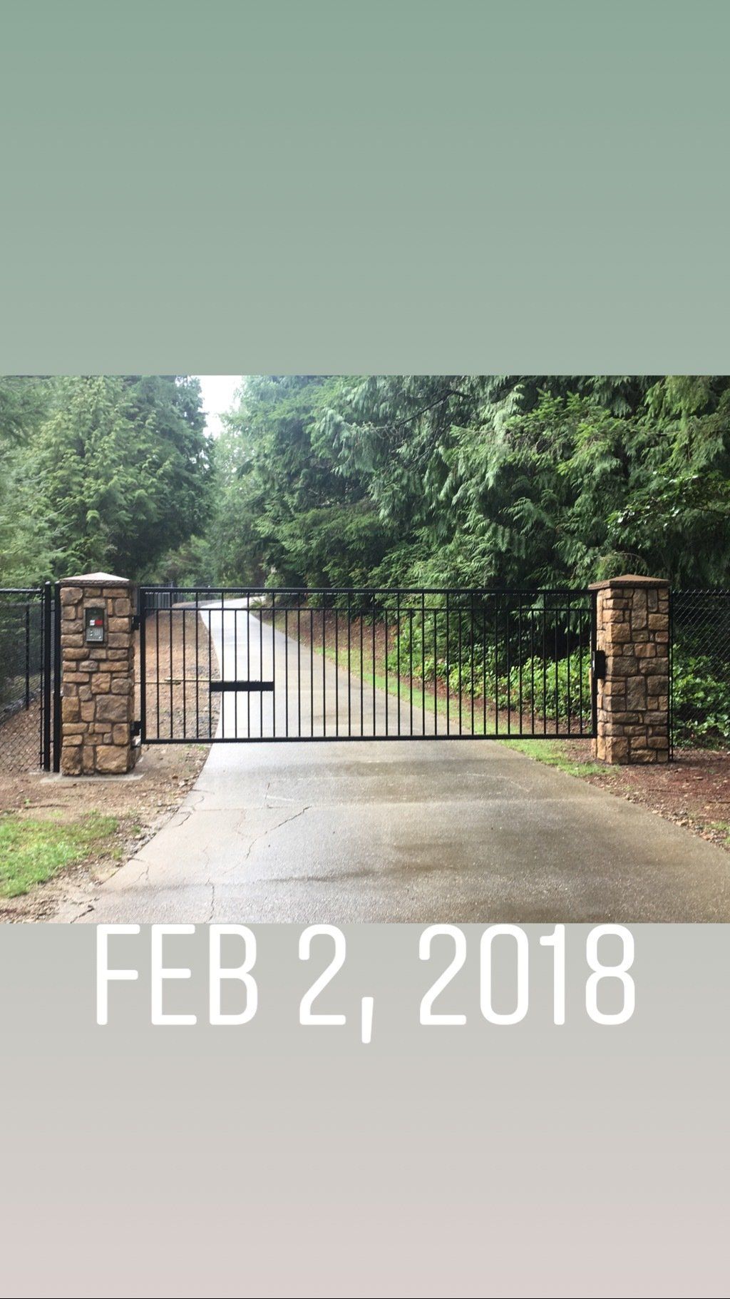 Gated driveway entrance with brick pillars and iron fence, surrounded by trees, dated Feb. 2, 2018