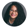 Portrait of a smiling woman with curly hair, glasses, and a necklace on a white background