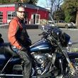 Person sitting on a blue motorcycle in front of a red building on a sunny day