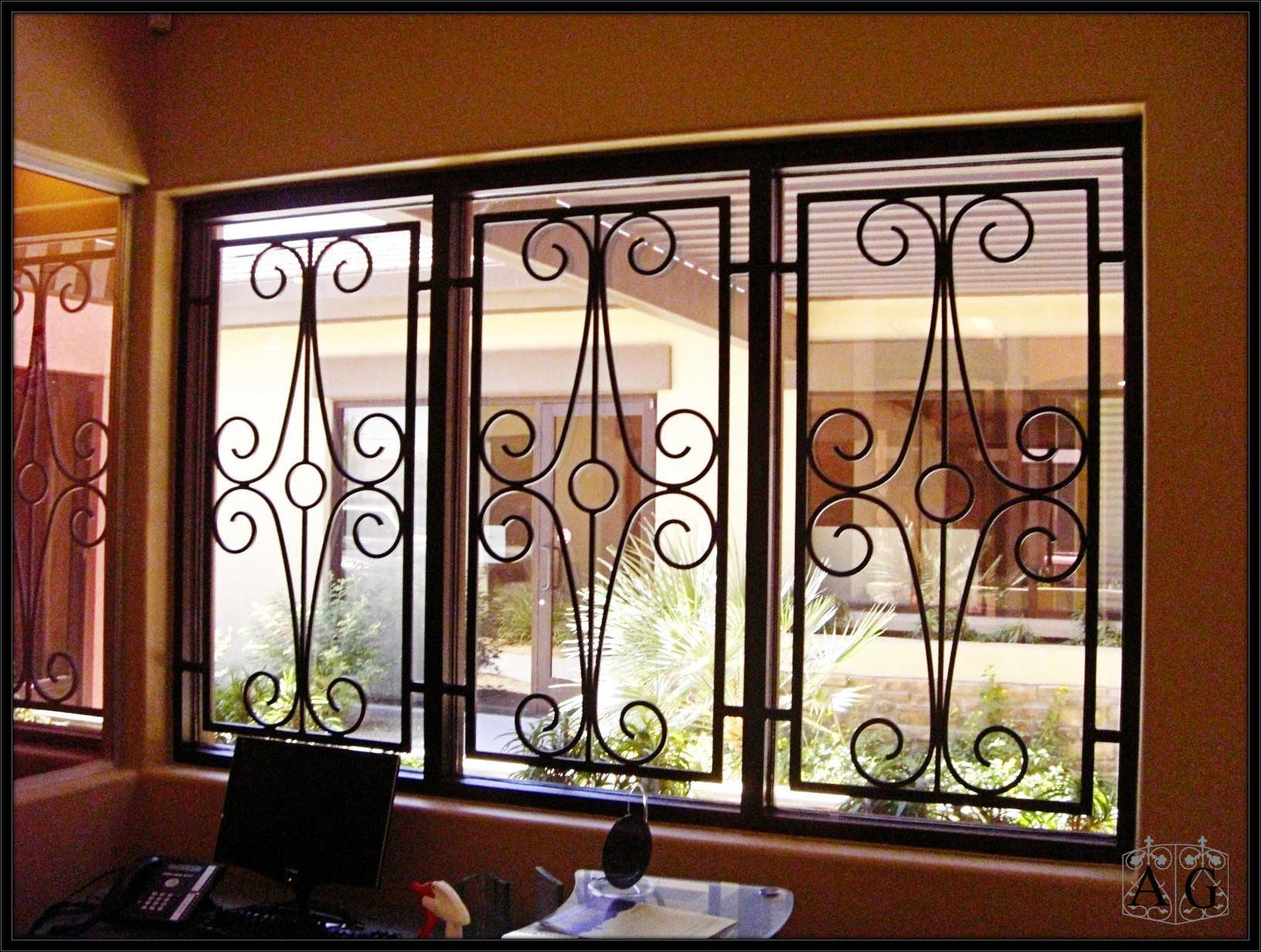 Window with decorative black iron bars overlooking a sunlit courtyard and building exterior