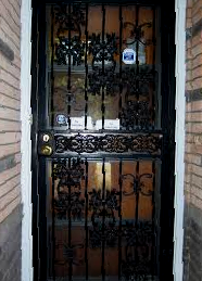 Black wrought-iron security door with glass panels and a brass knob at a brick entryway