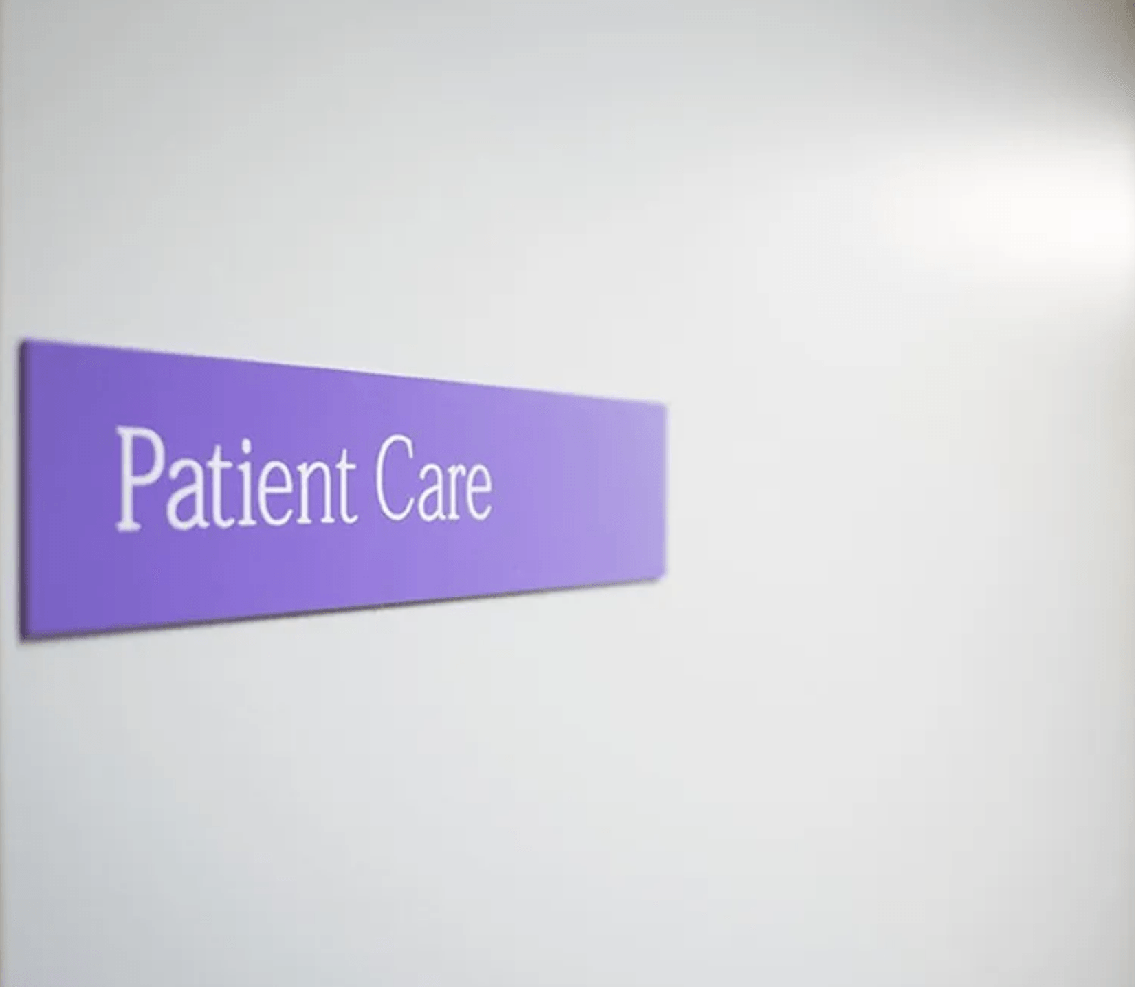 A purple sign on a white wall says patient care
