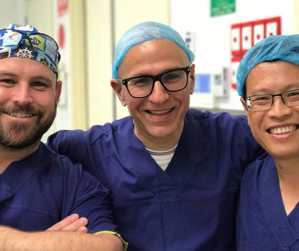 Three men wearing scrubs and hats are posing for a picture