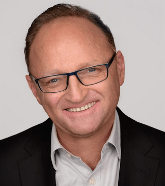 A man wearing glasses and a suit is smiling for the camera.