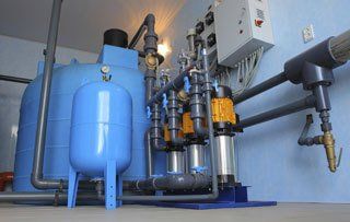 Blue water treatment equipment in a utility room; includes tanks, pipes, pumps, and control panel.