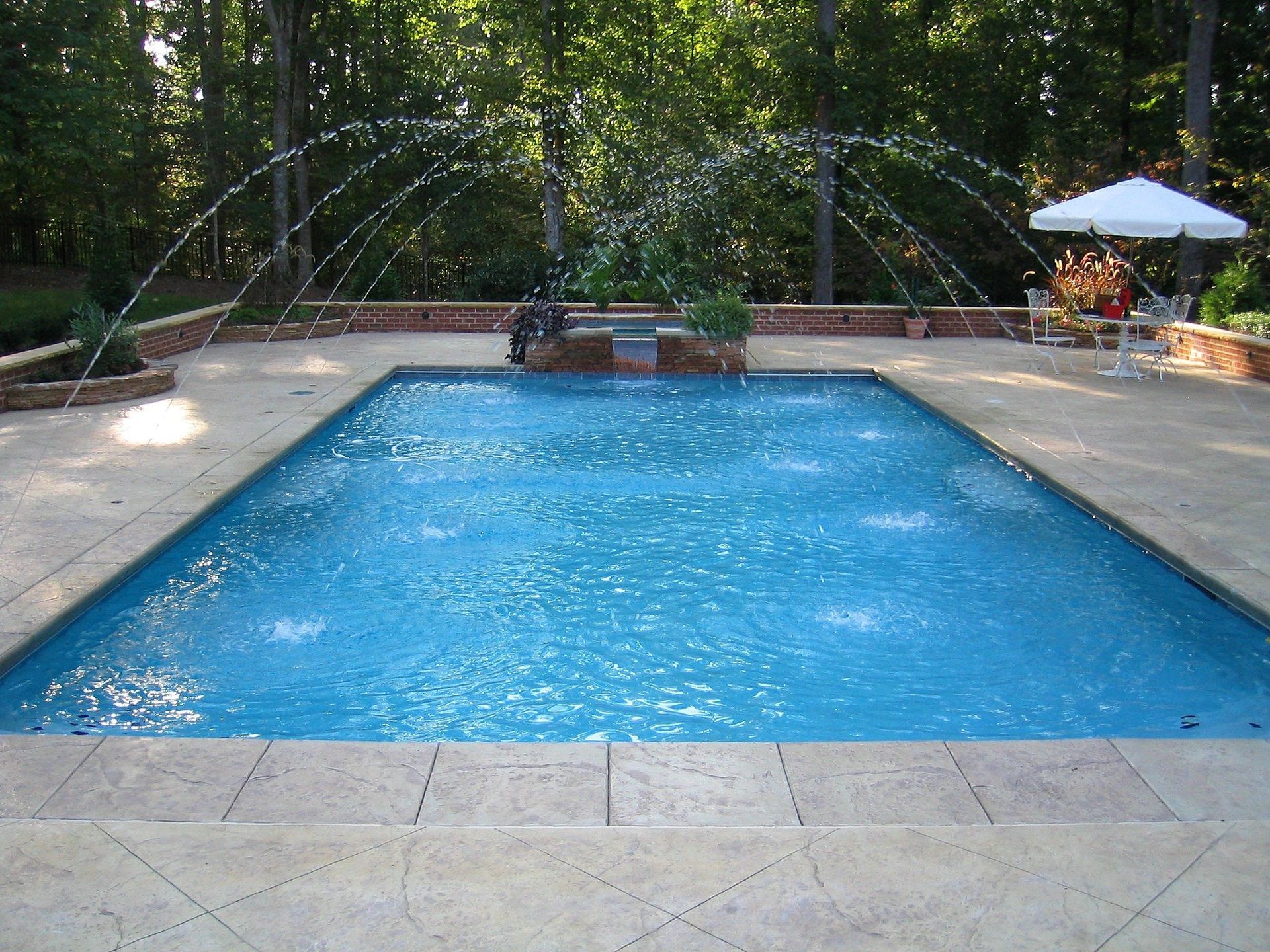 A rectangular pool with fountains, surrounded by a stone patio and landscaping.