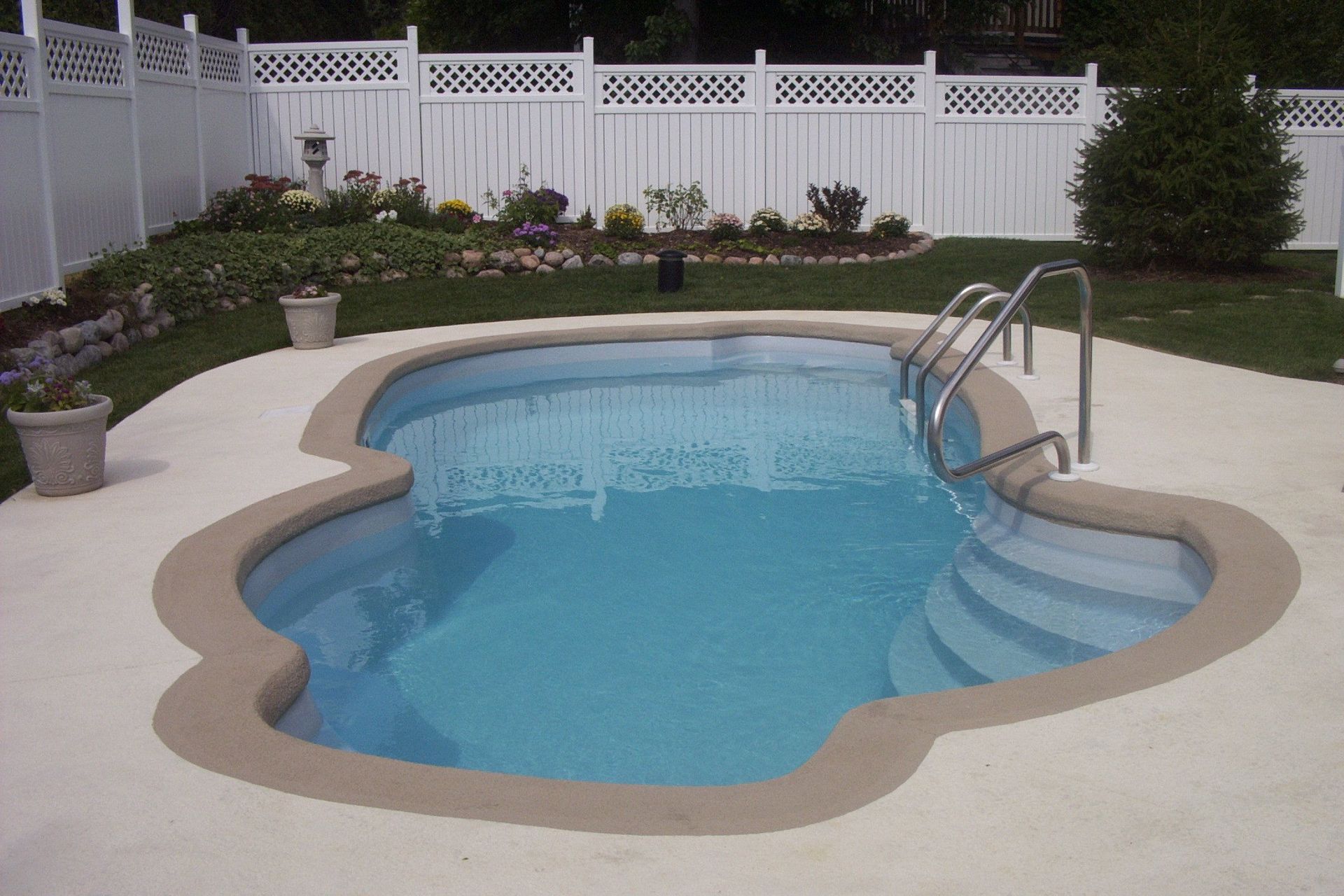 Swimming pool with light blue water, surrounded by concrete and a white fence.