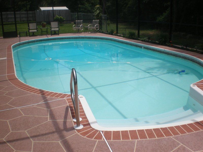 Swimming pool with brick border, patio, and metal handrail.