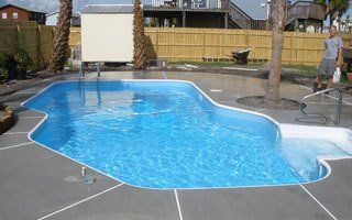 Swimming pool, with blue water, concrete surround, man standing nearby.