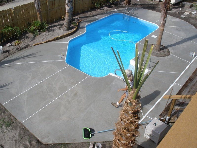 Overhead view of a pool with a gray concrete patio and a person near a palm tree.