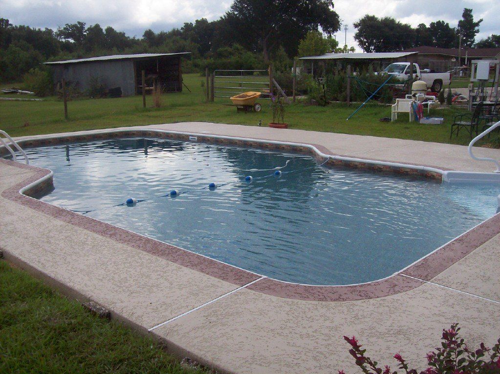 Swimming pool in backyard with surrounding concrete, two sheds, and a vehicle.