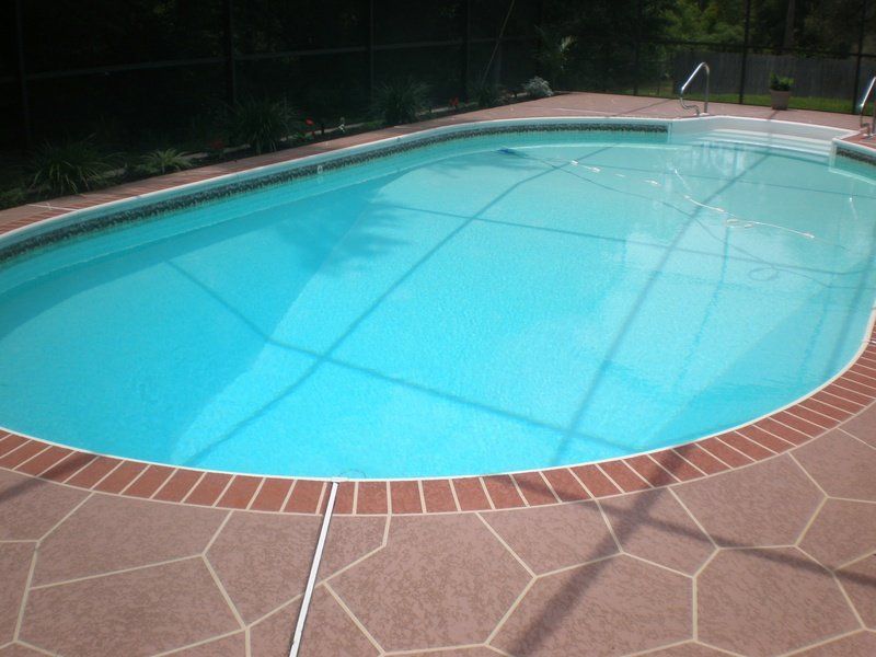 Oval swimming pool with a safety cover, surrounded by a brick-lined deck.
