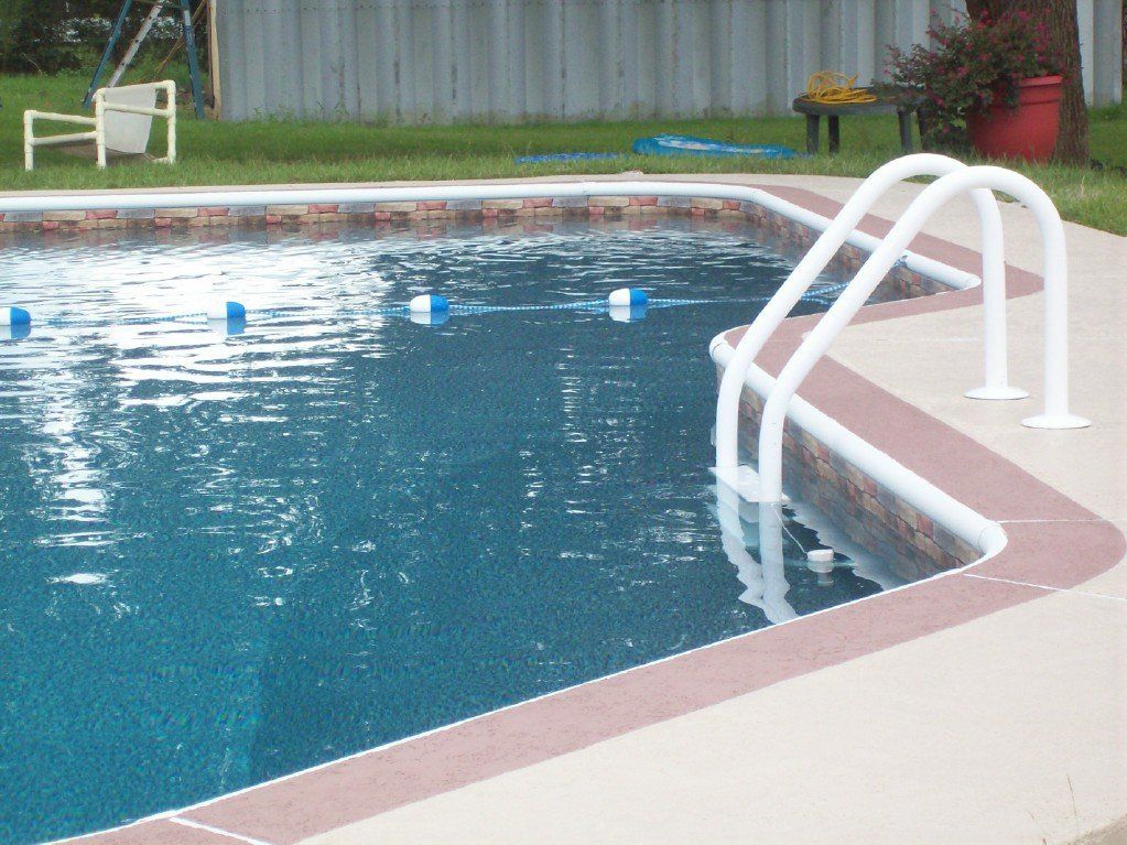 Swimming pool with white ladder, blue water, and tan concrete border.