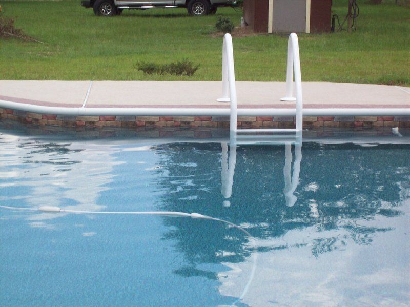 Swimming pool with white ladder, brick coping, and a grassy background.