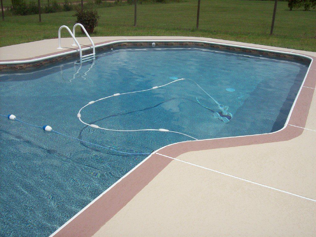 Swimming pool with clear blue water and concrete border. A pool cleaner is in use.