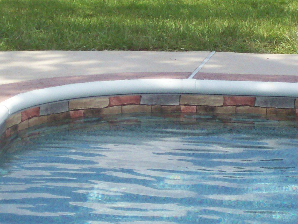 Pool edge with brick-like tiles, concrete coping, and grassy lawn in the background.