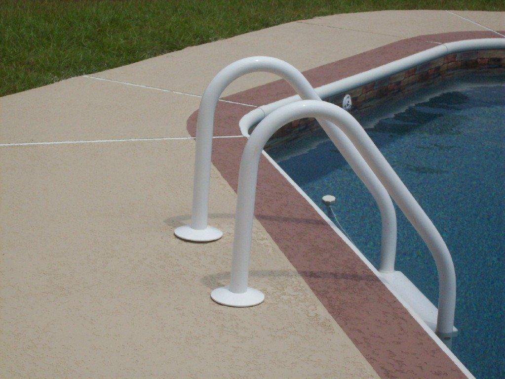 Pool ladder with white handrails on a beige pool deck, next to a pool with blue water.