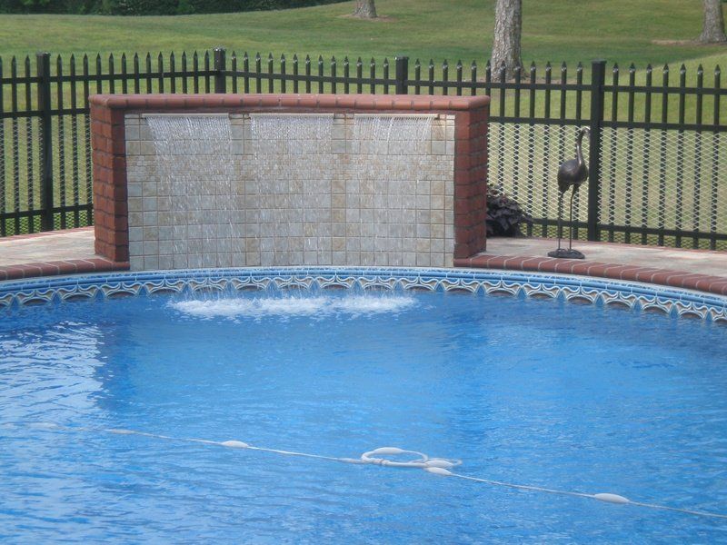 Pool with brick waterfall feature; black fence and lawn in background.