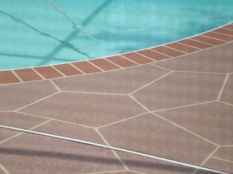 Pool edge with reddish-brown decorative paving stones, turquoise water, and brick border.