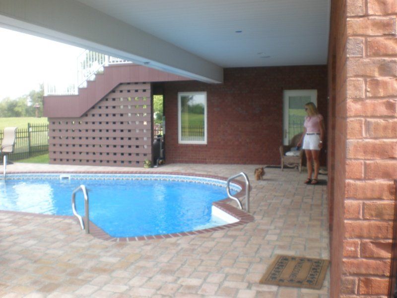 Poolside area with a pool, brick walls, a person standing near a door, and stairs leading up.