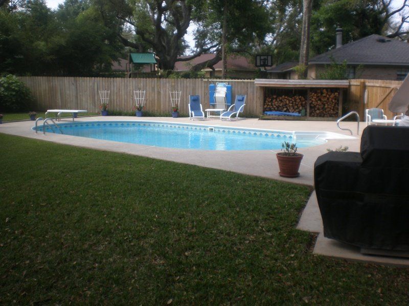 Backyard with a swimming pool, wooden fence, grass, lounge chairs, and a wood storage shed.