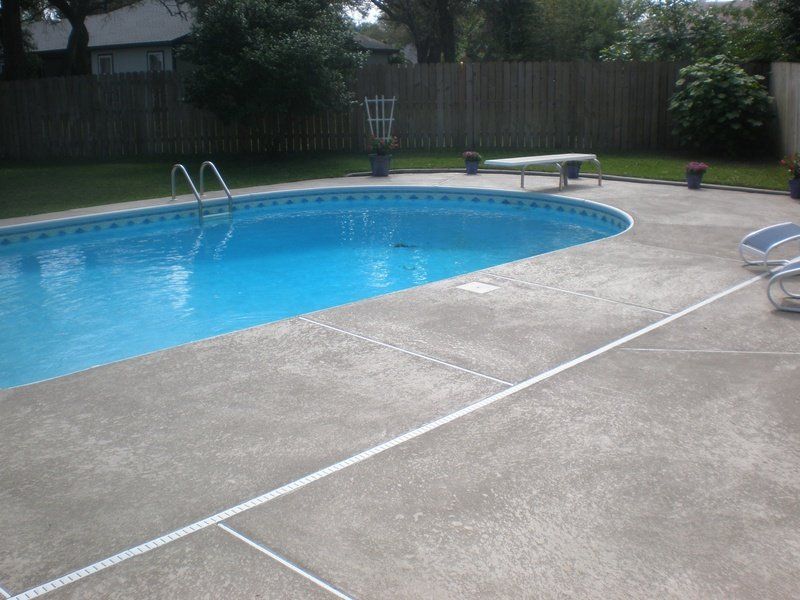 Swimming pool with blue water and concrete deck; backyard setting.