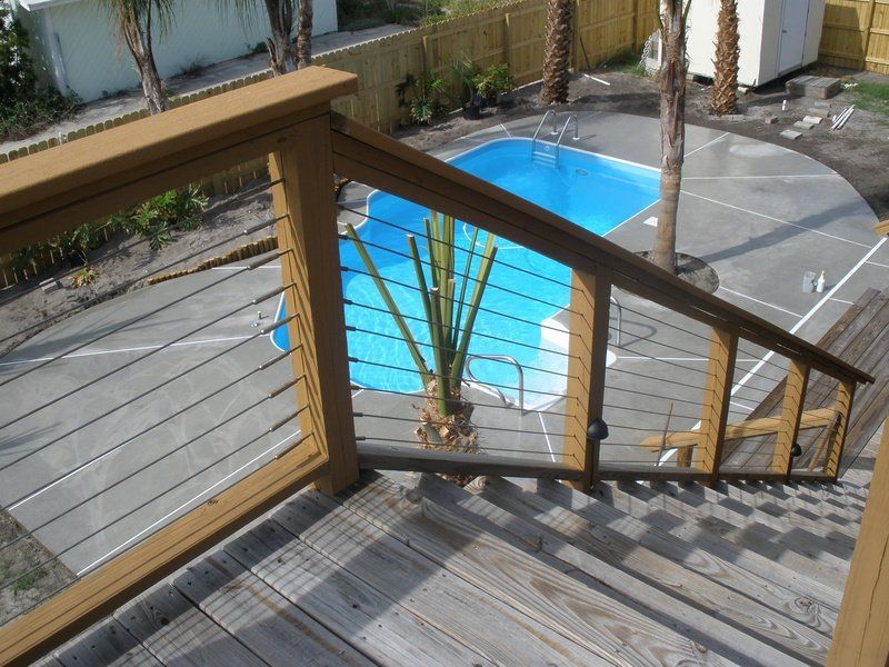 Wooden deck with cable railings overlooks a pool.