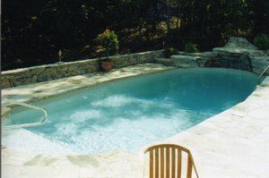 Swimming pool with stone deck and waterfall feature. Chair in foreground.
