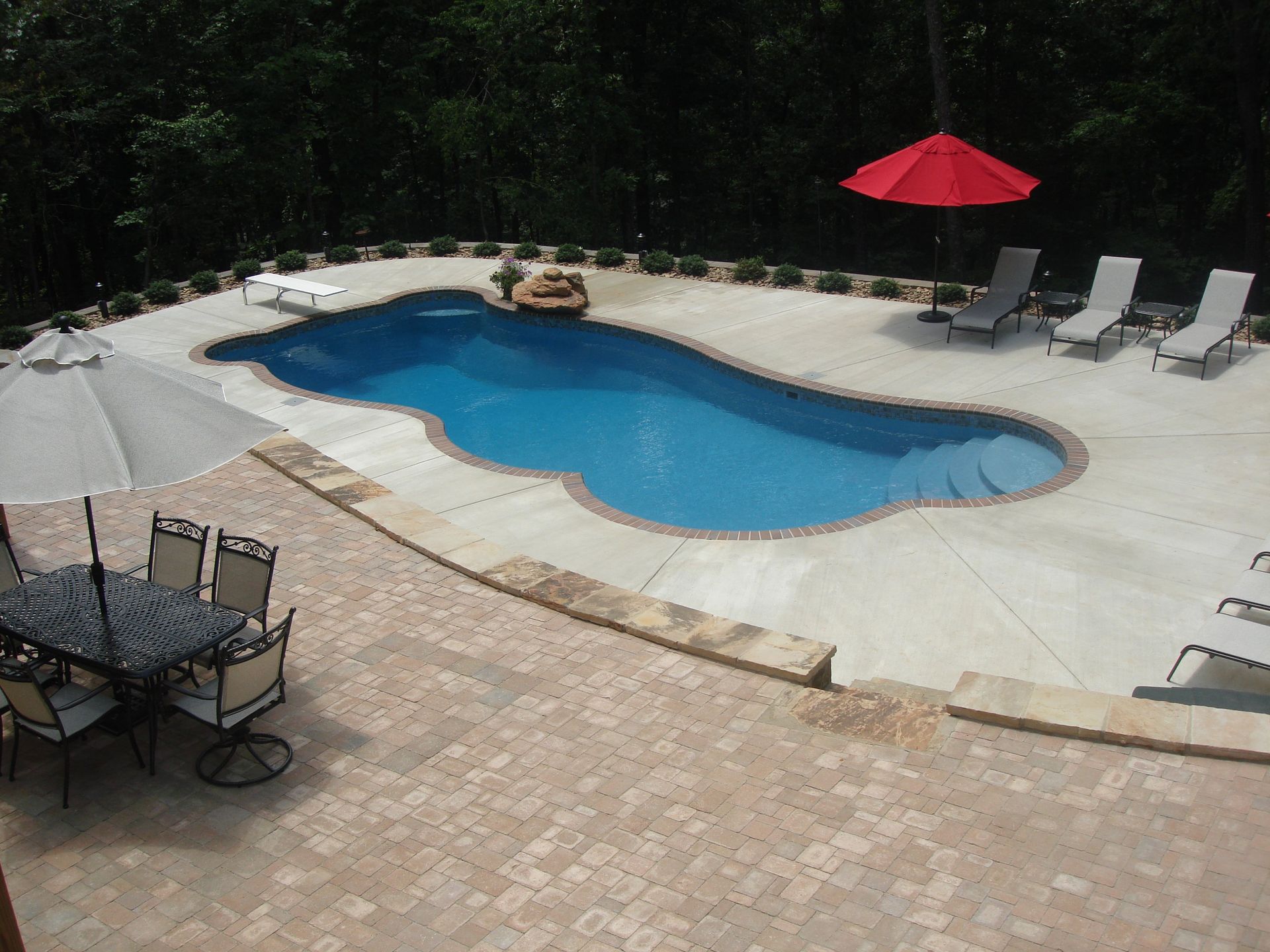 Swimming pool with surrounding patio, lounge chairs, red umbrella, and dining table.