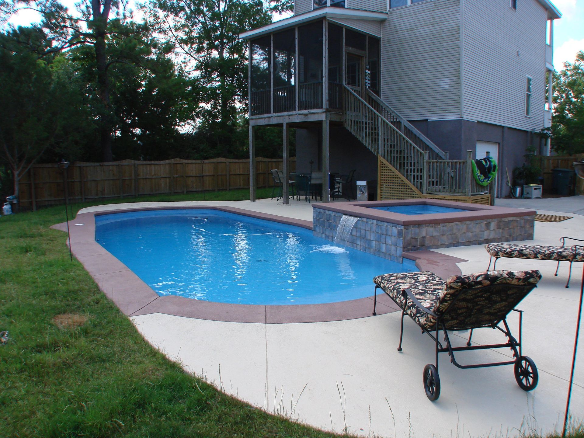 Swimming pool and hot tub next to a house with a screened porch and stairs.