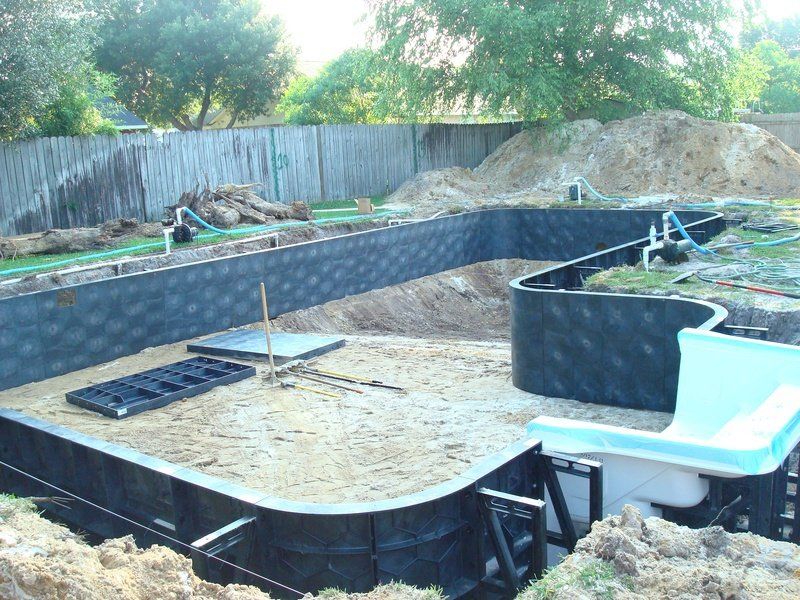 Pool construction site; excavated area with black pool walls, sand base, plumbing visible, and a dirt pile.