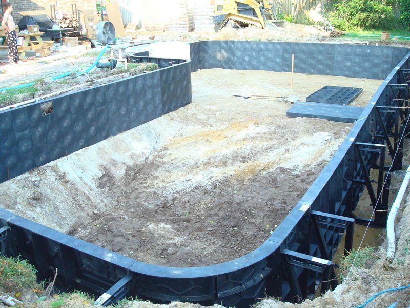 Pool construction site, dirt excavation with black modular wall framework.