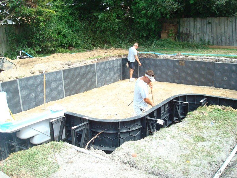 Workers installing a vinyl liner pool; excavating, leveling sand, and assembling walls in a yard.