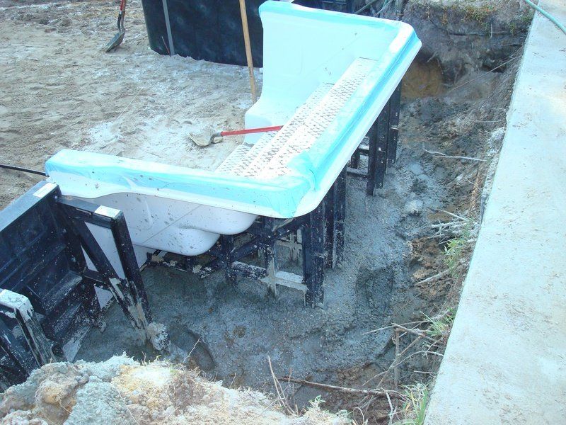 Pool construction: A light blue slide frame sits over a concrete foundation, in a partially excavated area.