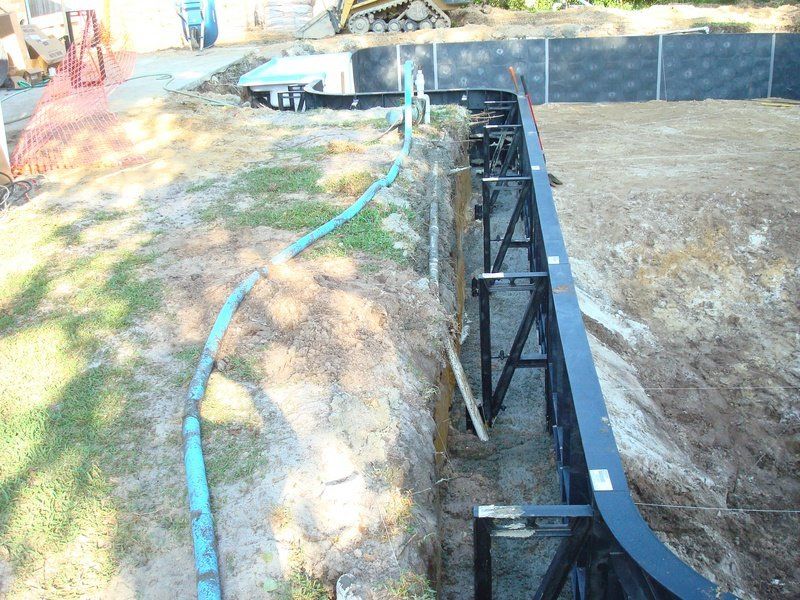 Construction site with trench, black metal supports, and blue hose along the side.