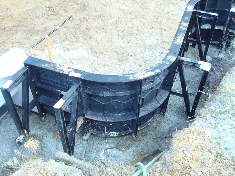 Black pool formwork installed in a curved shape, with support braces, set in gravel and dirt.
