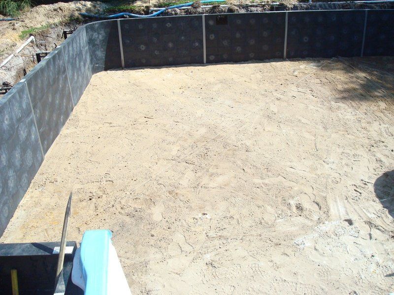 Pool construction site with sand base, dark walls, and a light blue object in the foreground.