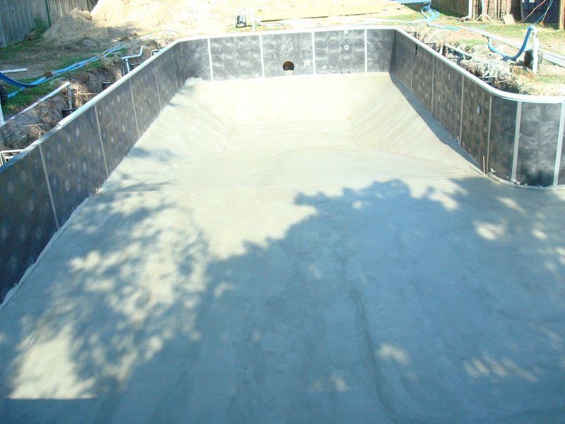Newly constructed rectangular swimming pool basin with concrete floor and walls.