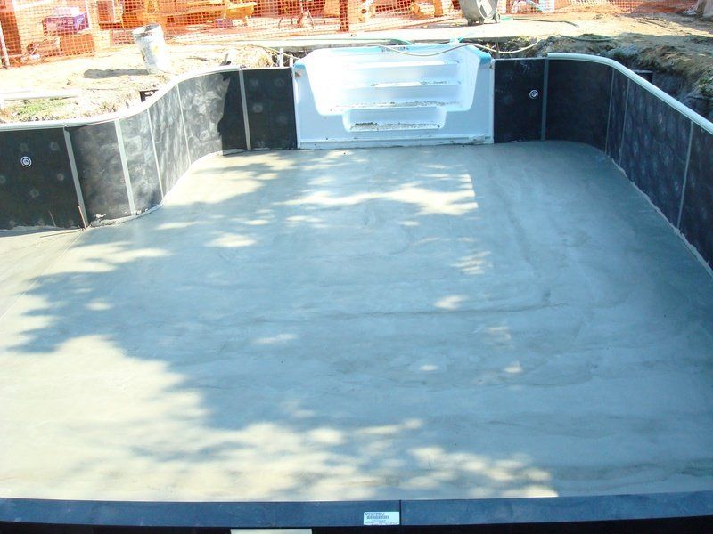 Construction site of a pool, concrete floor with white steps. Walls are lined with black material.