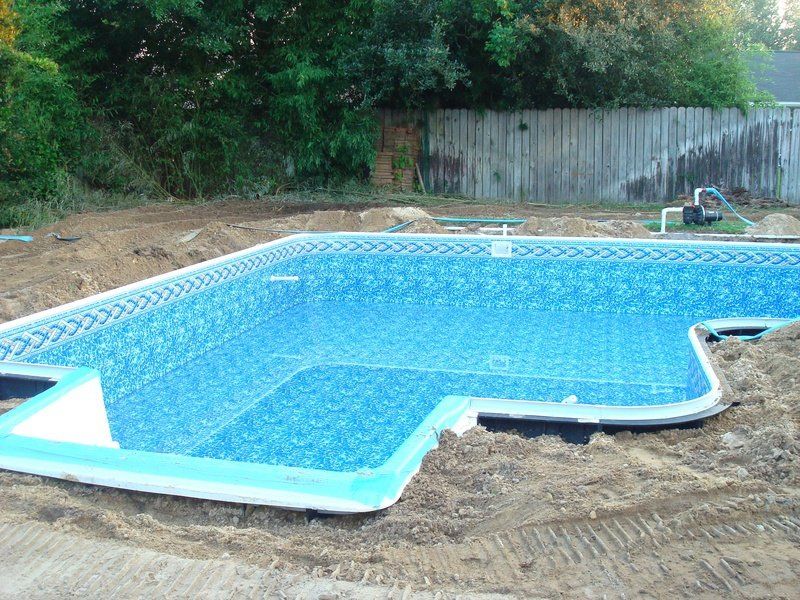 Empty, newly constructed swimming pool with blue tile interior, surrounded by dirt.