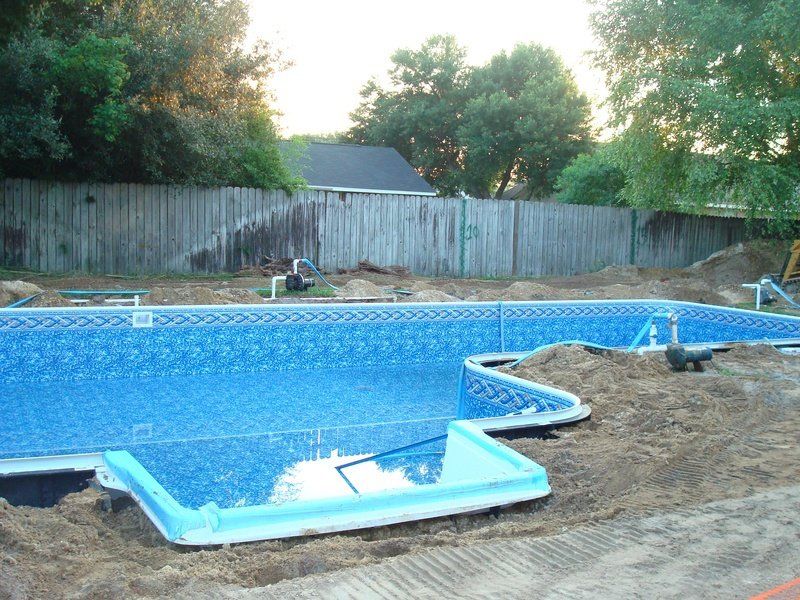 Pool being built with blue patterned liner, dirt, and a wooden fence.