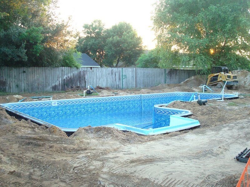 Newly constructed swimming pool with blue tiled interior, surrounded by dirt and construction equipment.